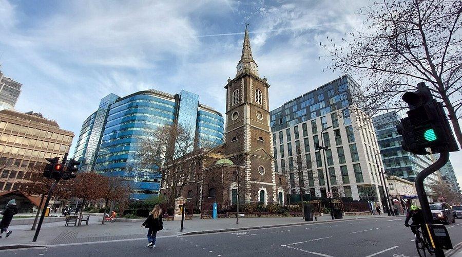 The spire of St Botolph without Aldgate rising between the glass office buildings on Aldgate High Street.