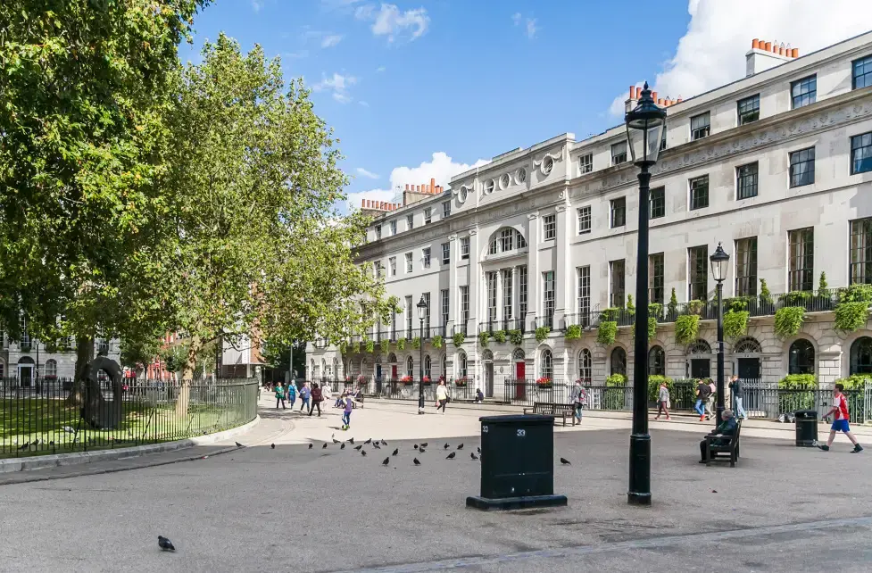 A stucco fronted Georgian crescent facing a garden square near Euston, with plane trees behind the railings.