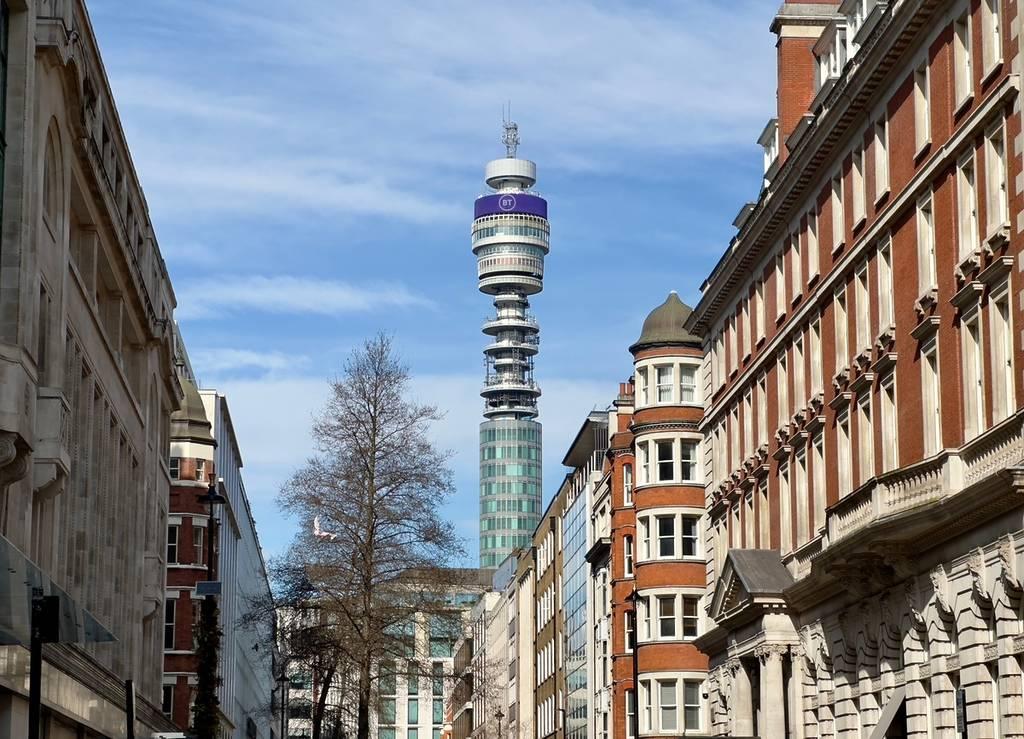 The BT Tower seen down a Fitzrovia street, framed by red brick mansion blocks and stone frontages.