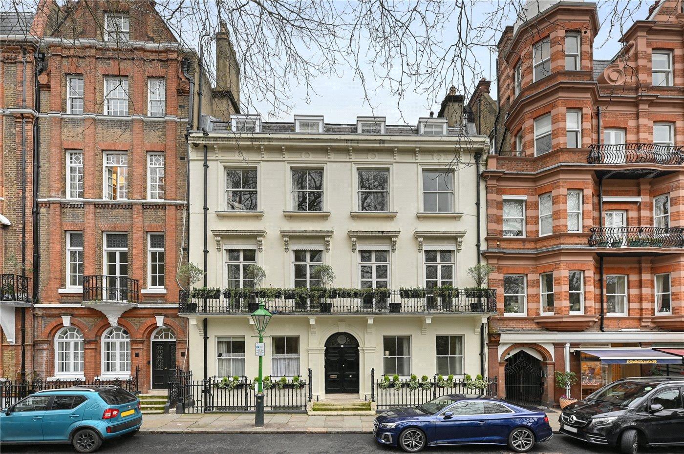 A stucco fronted townhouse on Kensington Square between red brick mansion blocks, with railings and a first floor balcony.