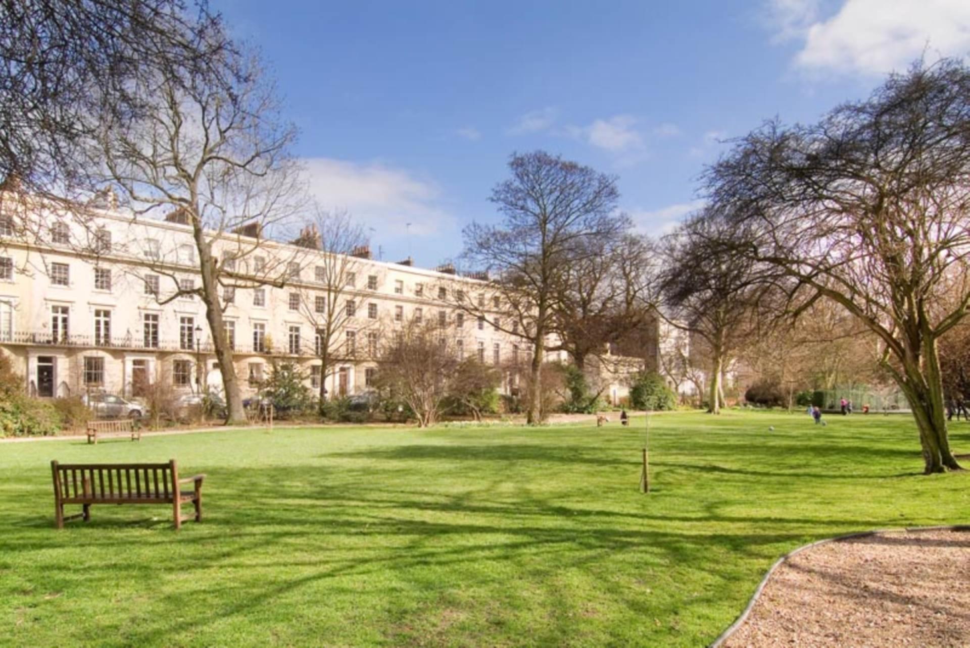 A stucco crescent of Central London flats seen across the private garden square in front of it.