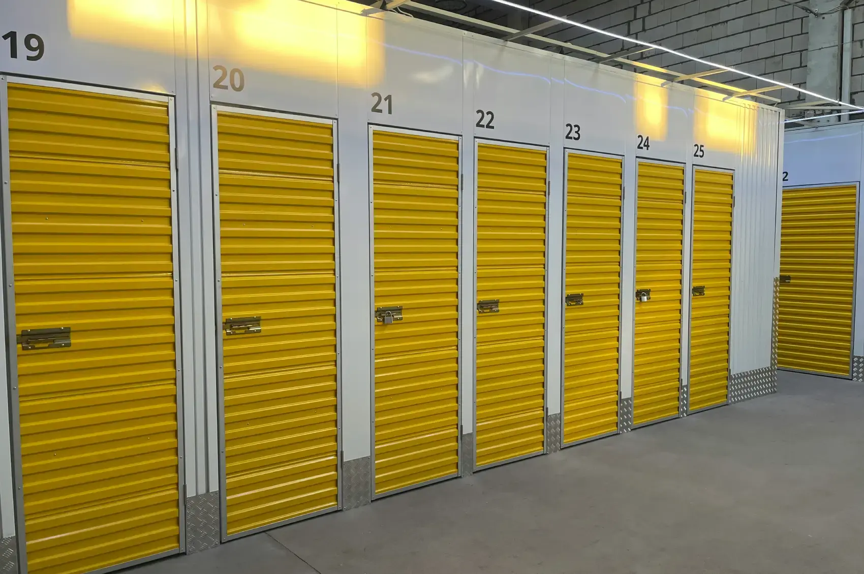 A row of numbered self storage units with yellow roller doors in a clean, lit facility.